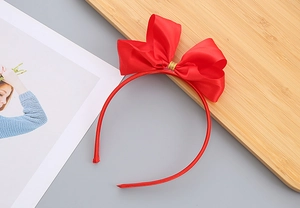 Dettaglio del cerchietto con fiocco in raso rosso e filo dorato su supporto in legno