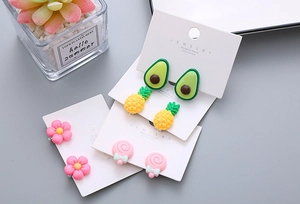Detailed macro of resin earrings with avocado, pineapple, and floral designs on display cards
