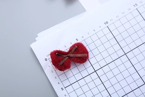 Close-up of red plush bow hair clip with brown ribbon detail on centimeter grid paper