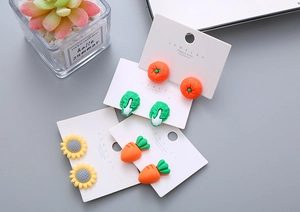 Detail showing colorful resin fruit and flower clip-on earrings for kids on a card