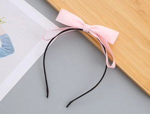 Detail shot of a layered light pink fabric bow headband for girls on a soft gray surface