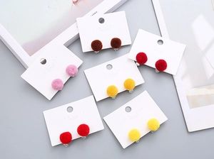 Detail view of colorful plush pom-pom clip-on earrings for kids in six vibrant shades