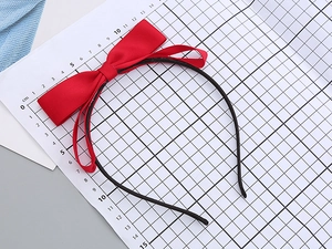 Detail view of a large red satin bow headband on a scale ruler for size reference