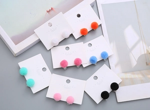Close-up of assorted colorful plush ball clip-on earrings displayed on jewelry cards