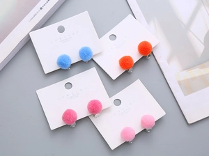 Close-up of colorful plush ball clip-on earrings for kids in various soft pastel shades