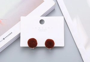 Detail of dark brown plush pompom clip-on earrings with 925 silver posts on display card