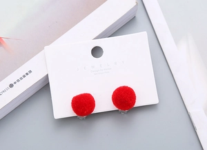 Macro view of plush red pompom clip-on earrings on a white jewelry display card