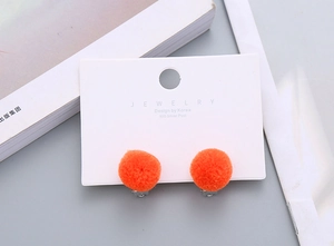 Detailed view of orange fuzzy ball clip-on earrings for girls on a jewelry card