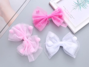 Dettaglio di tre fiocchi per capelli in rete con pompon nei colori rosa e bianco