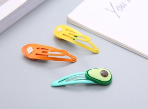 Dettaglio delle clip per capelli in resina con avocado e fiori su forcine metalliche