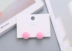 Detail of pink pompom earrings with 925 silver needles on a white jewelry card