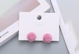 Close-up of pink fluffy pompom clip-on earrings on a white Korean design jewelry card