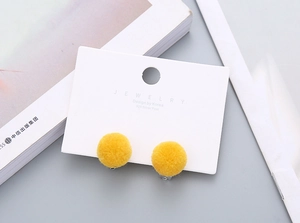 Detail of yellow plush pom-pom earrings featuring 925 silver posts on a display card
