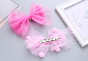 Dettaglio di fermagli per capelli a fiocco in tulle rosa con pompon e clip in metallo