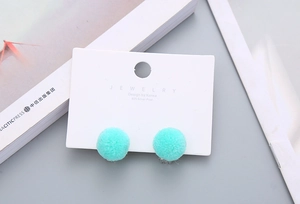 Close-up of soft mint green plush pom pom ear clips on a jewelry card for children