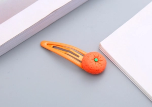 Dettaglio di un grazioso fermaglio per capelli arancione con decorazione in resina a forma di arancia