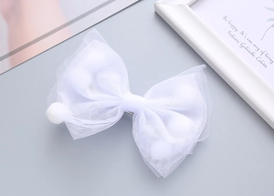 Dettaglio di fiocco in tulle bianco con pompon di peluche e clip a coccodrillo