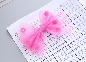 Dettaglio del fermaglio per capelli a fiocco rosa con pompon su griglia graduata