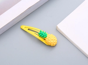 Dettaglio di un fermaglio per capelli in metallo giallo con ciondolo a forma di ananas