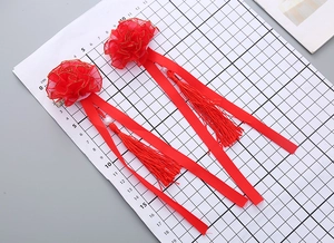 Close-up of red floral hair clips with tassels and pearls on a grid measuring mat