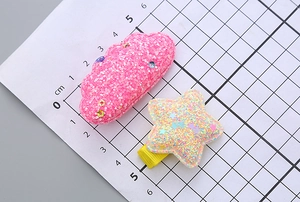 Close-up of glittery pink cloud and yellow star hair clips on a centimeter scale board