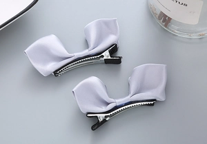 Détail de pinces à cheveux à nœuds en satin lilas avec socles en métal sur fond gris