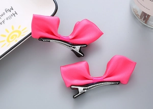 Détail de deux pinces à cheveux à nœud en satin rose fuchsia avec pinces crocodiles