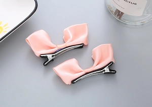 Gros plan de barrettes à nœud en satin rose avec clips crocodiles sur fond gris