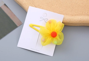 Detail of yellow mesh flower hair clip with orange pompom on a white display card