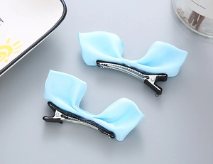 Détail de deux barrettes à nœuds en satin bleu clair avec pinces crocodile en métal