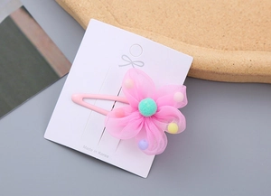Close-up of pink mesh flower hair clip with green pom-pom and colorful beads on white card
