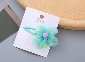 Detail of mint green mesh flower hair clip with fuzzy pom center on a white display card