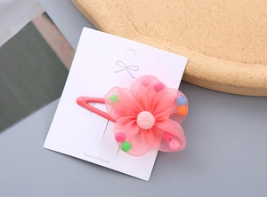 Close-up of a pink mesh flower hair clip with colorful beads and soft pom-pom detail