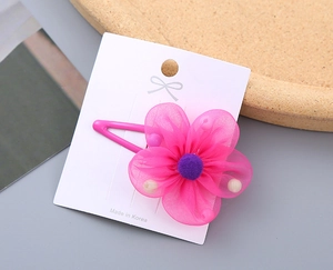 Detail of pink organza flower hair clip with purple pom-pom on display card