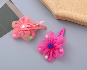 Detail of mesh flower hair clips in coral and rose pink with colorful pom-poms on BB clips