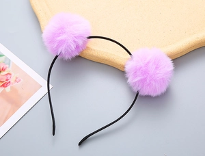 Close-up of cute purple plush pom-pom hairband for girls on a textured display tray