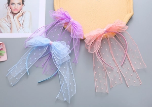 Close-up of three mesh polka dot bow headbands with long ribbons in purple, blue and pink