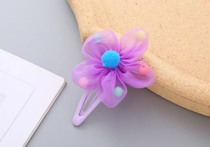 Detail of purple mesh flower hair clip with blue pompom and colorful beads on metal clip