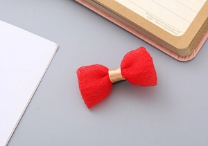 Close-up of red bubble gauze bow hair clip with gold satin ribbon detail on a flat surface