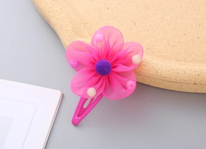 Close-up of pink mesh flower hair clip with purple fuzzy pompom and tiny pearl beads