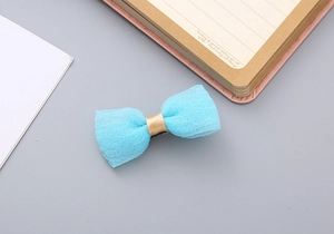 Close-up of a light blue mesh bow hair clip with a golden ribbon center on a desk
