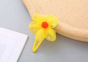 Close-up of yellow floral hair clip with mesh petals and colorful mini pom-poms