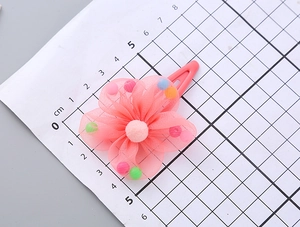 Detail showing 5cm pink mesh flower hair clip with colorful pom-poms on scale ruler