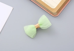 Close-up of light green seersucker bow hair clip with gold satin center on gray desk