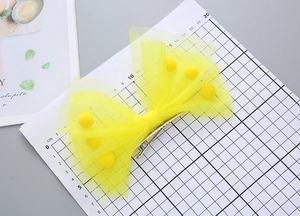 Détail d'une pince à cheveux nœud en résille jaune avec pompons sur plateau de mesure