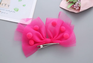 Détail d'un nœud à cheveux en tulle rose avec pompons doux et pince crocodile en métal