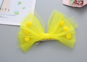 Détail d'une pince à cheveux nœud en tulle jaune ornée de pompons et clip en métal
