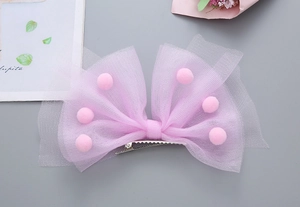 Détail de la pince à cheveux noeud en tulle rose avec pompons duveteux décoratifs