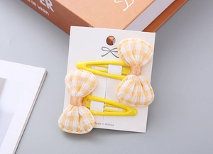 Close-up of yellow checkered bow hair clips on white card holder with warm aesthetic decor