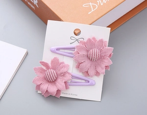 Detail of two pink fabric flower hair clips with striped buttons on purple metal BB clips